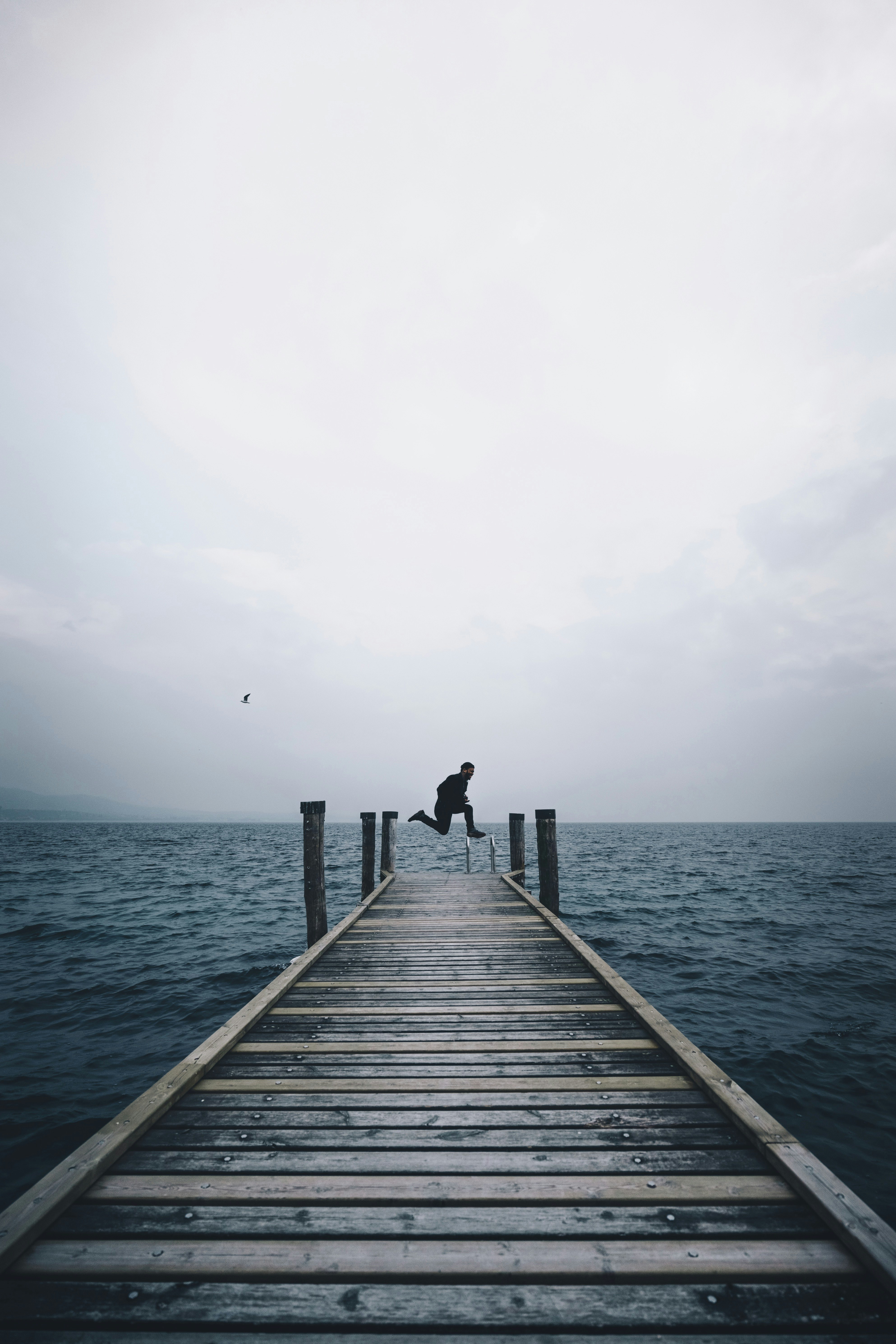 man jumping on brown wooden dock in middle of body of water